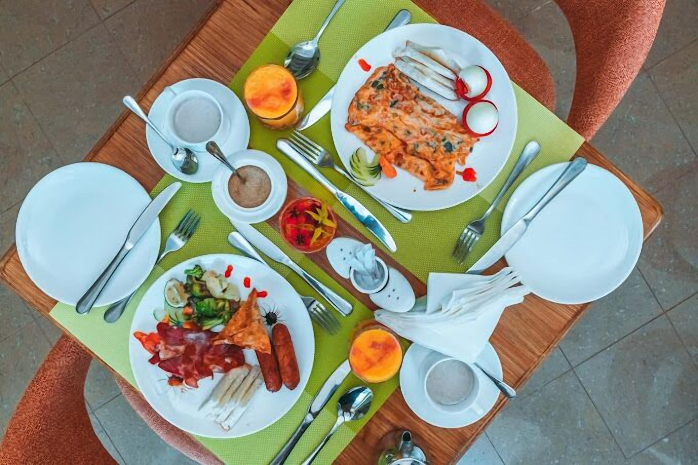 A dining table with plates of food, cutlery, and a green placemat.