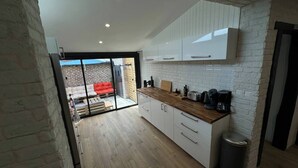 Une cuisine moderne avec des meubles blancs, un plan de travail en bois et une vue sur un espace extérieur aménagé avec des sièges rouges.