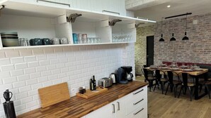 Une cuisine moderne avec des armoires blanches, un plan de travail en bois et un coin repas agrémenté d’un mur en briques et de luminaires suspendus.