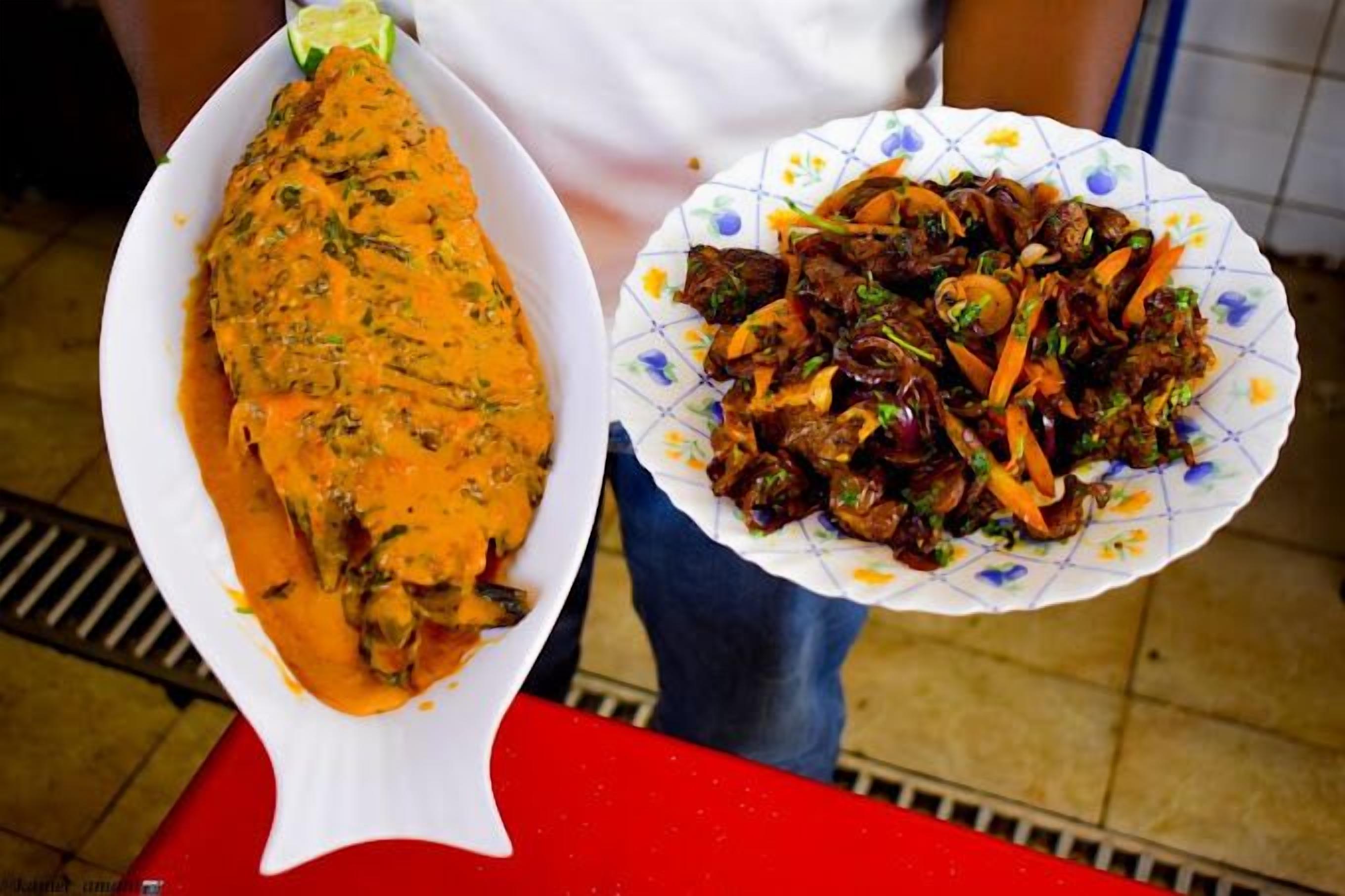 Una persona sosteniendo dos platos: uno con pescado en salsa y otro con salteado de verduras.