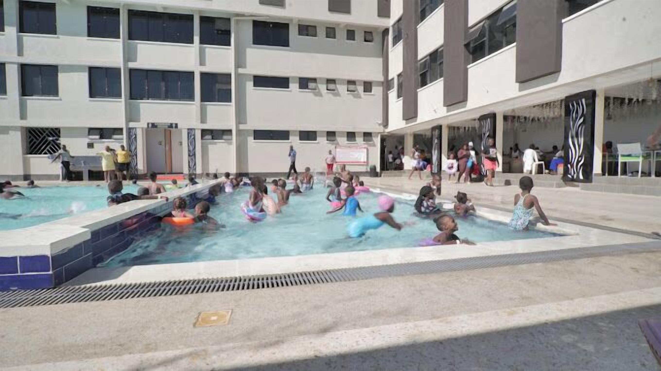 Zona de piscina con varias piscinas y gente nadando y divirtiéndose.