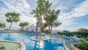 A swimming pool with lounge chairs, trees, and a building in the background.