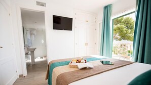 A hotel room with a bed, a TV, a window with curtains, and a bathroom visible in the background.
