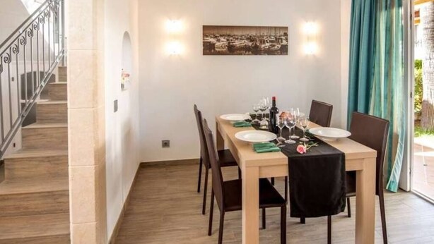 A dining area with a table set for four, chairs, a staircase, and a wall-mounted picture.
