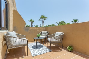 Un balcon avec deux fauteuils en osier, une petite table et un tapis à motifs.