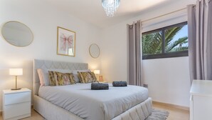 A bedroom with a bed, bedside tables, a chandelier, a window with curtains, and a framed picture on the wall.
