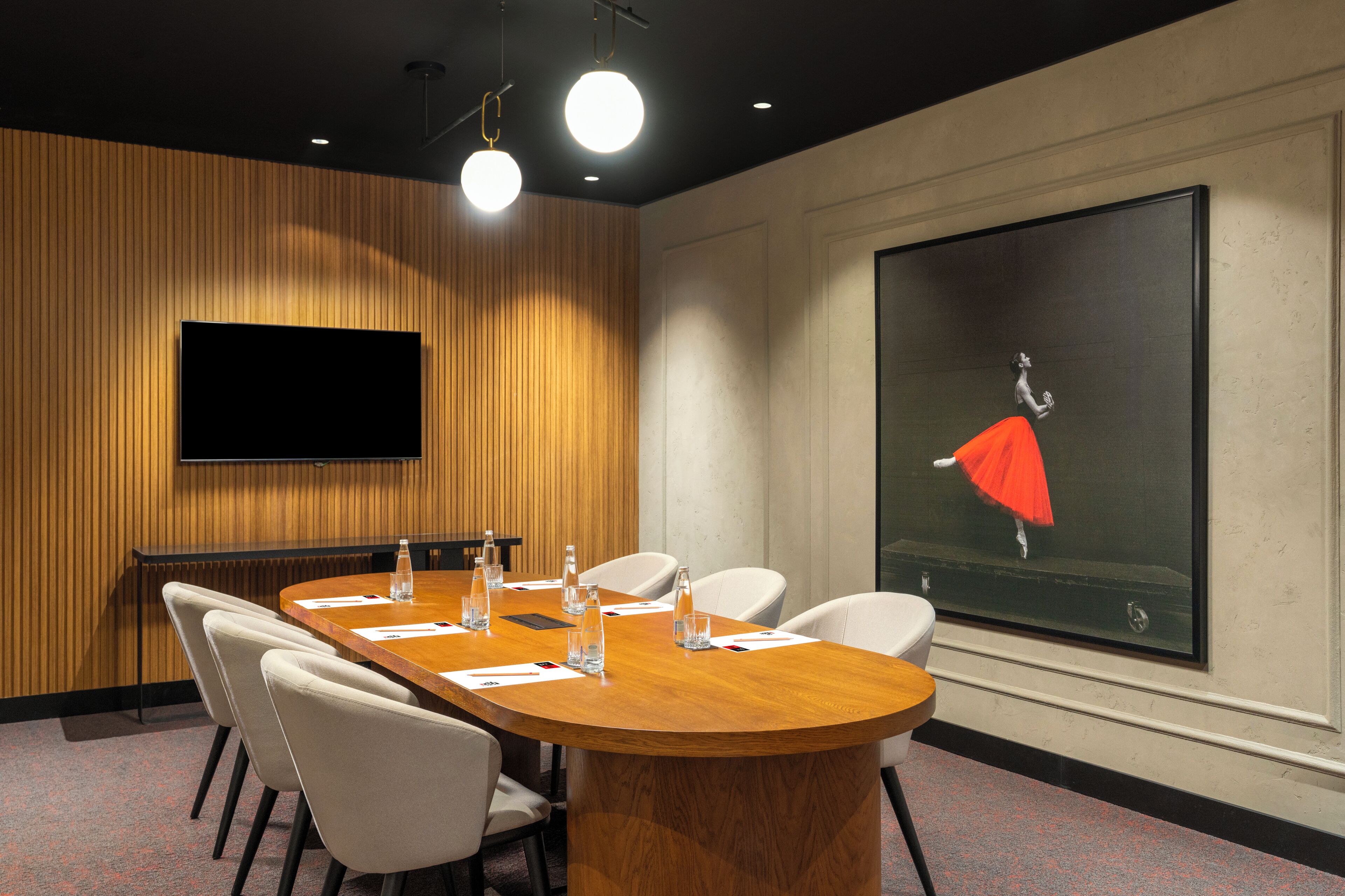 Ein Konferenzraum mit Holztisch, weißen Stühlen, einem Flachbildfernseher und einem großen Gemälde einer Tänzerin.