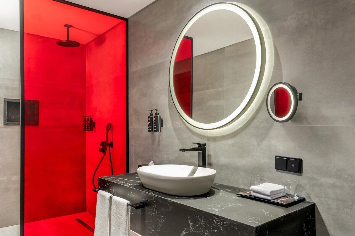 A modern bathroom with a round mirror, a white sink, and a red accent wall.