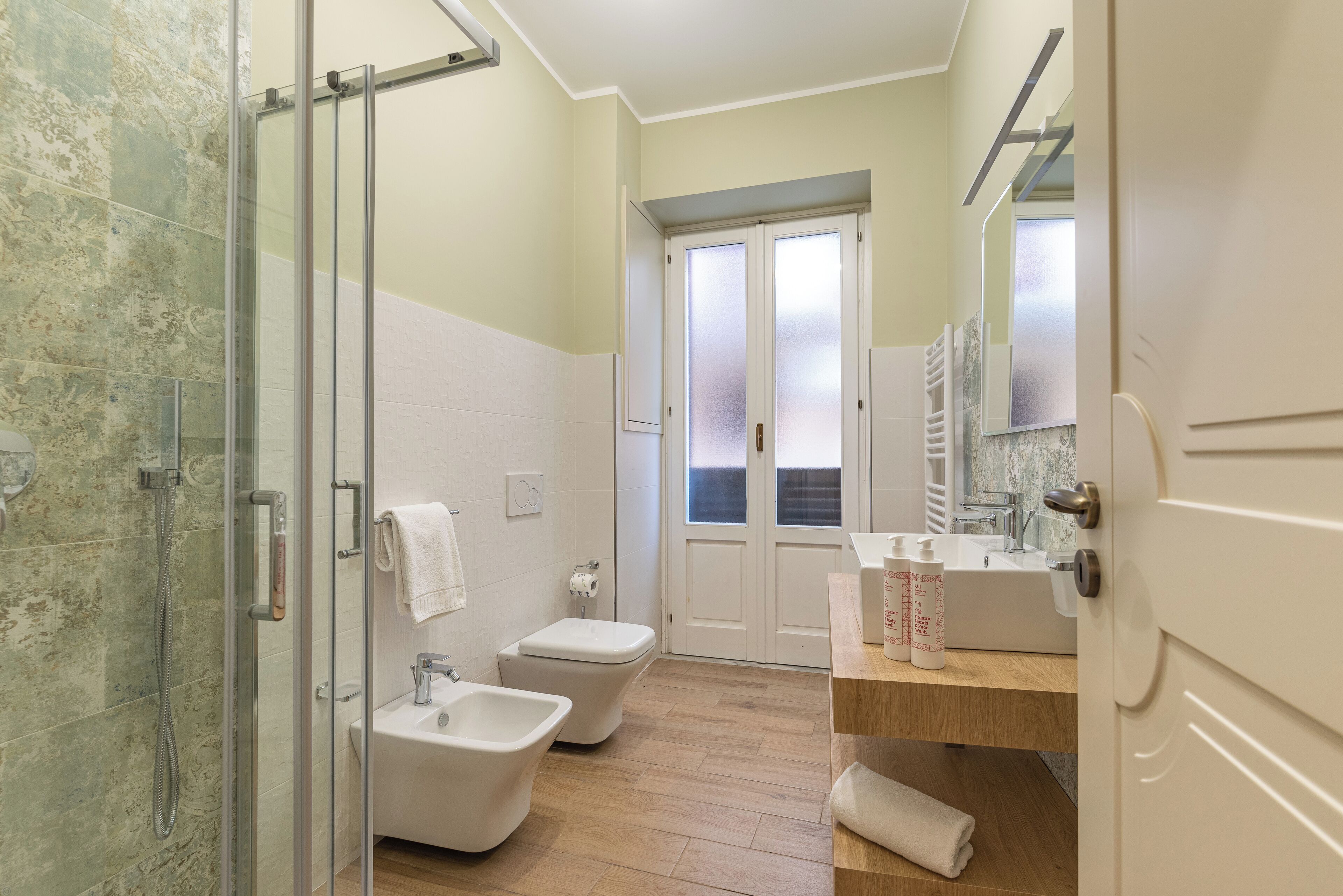 A bathroom with a glass shower enclosure, a bidet, a sink, and a mirror.
