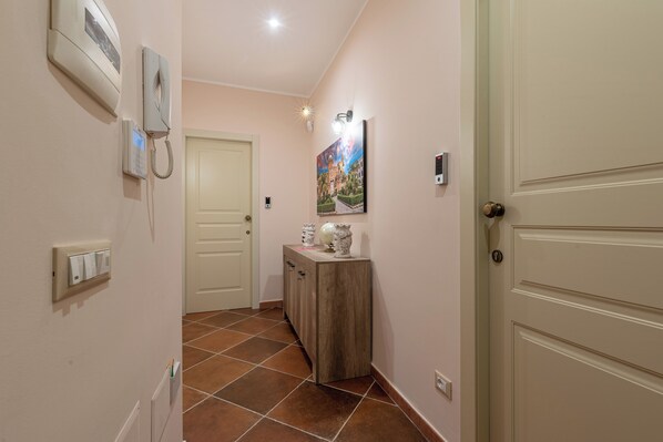 A hallway with a door, a wall-mounted phone, a light switch, and a painting.