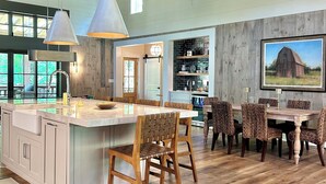 A spacious kitchen with a large island, wooden ceiling beams, and a dining area with wicker chairs. - Luxury Barn Retreat, Mountain Views and Creekside Calm (Ellijay)