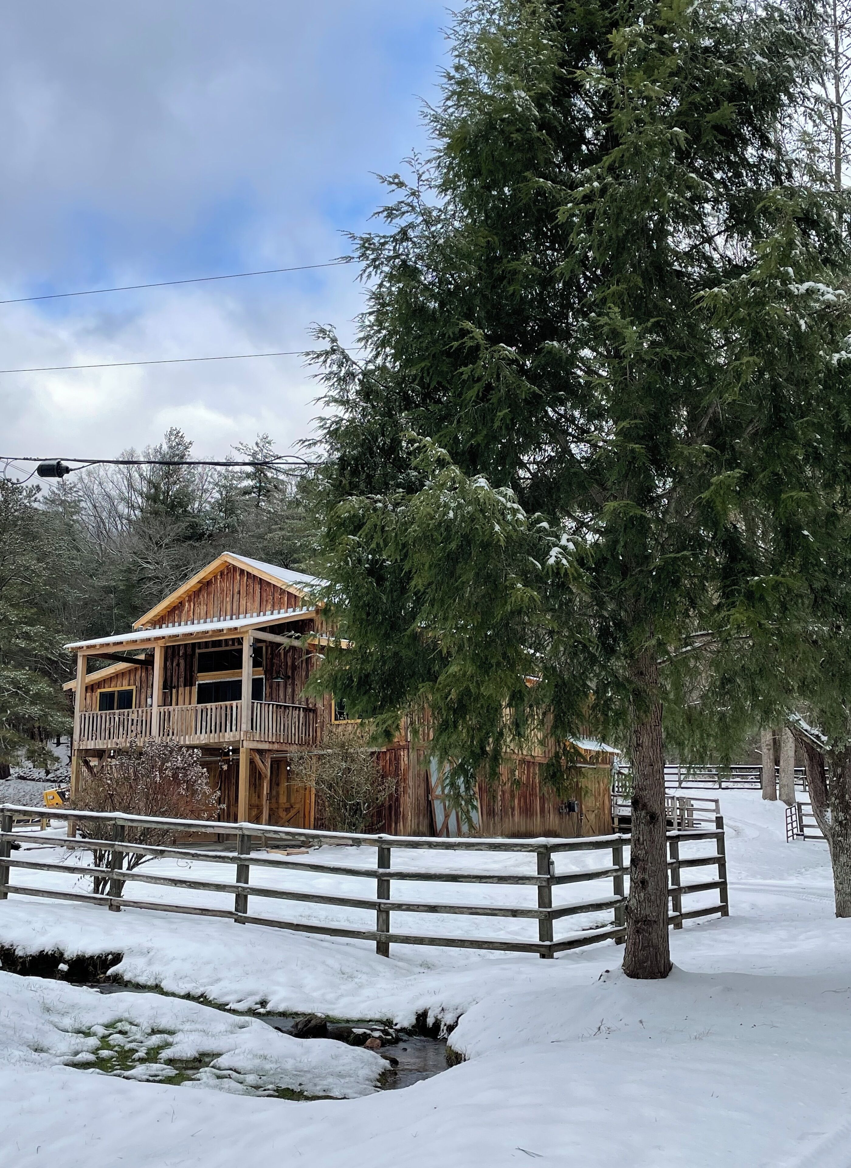 Une cabane en bois dotée d’un balcon, entourée d’arbres couverts de neige et d’une clôture en bois.