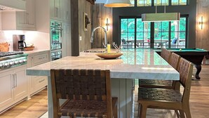 A spacious kitchen with a large island, wooden chairs, and a pool table in the background. - Luxury Barn Retreat, Mountain Views and Creekside Calm (Ellijay)