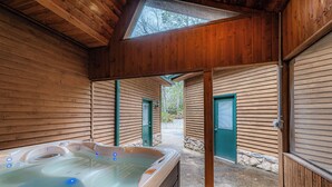 Una cabana de fusta amb banyera d'hidromassatge, parets de pedra i portes verdes.