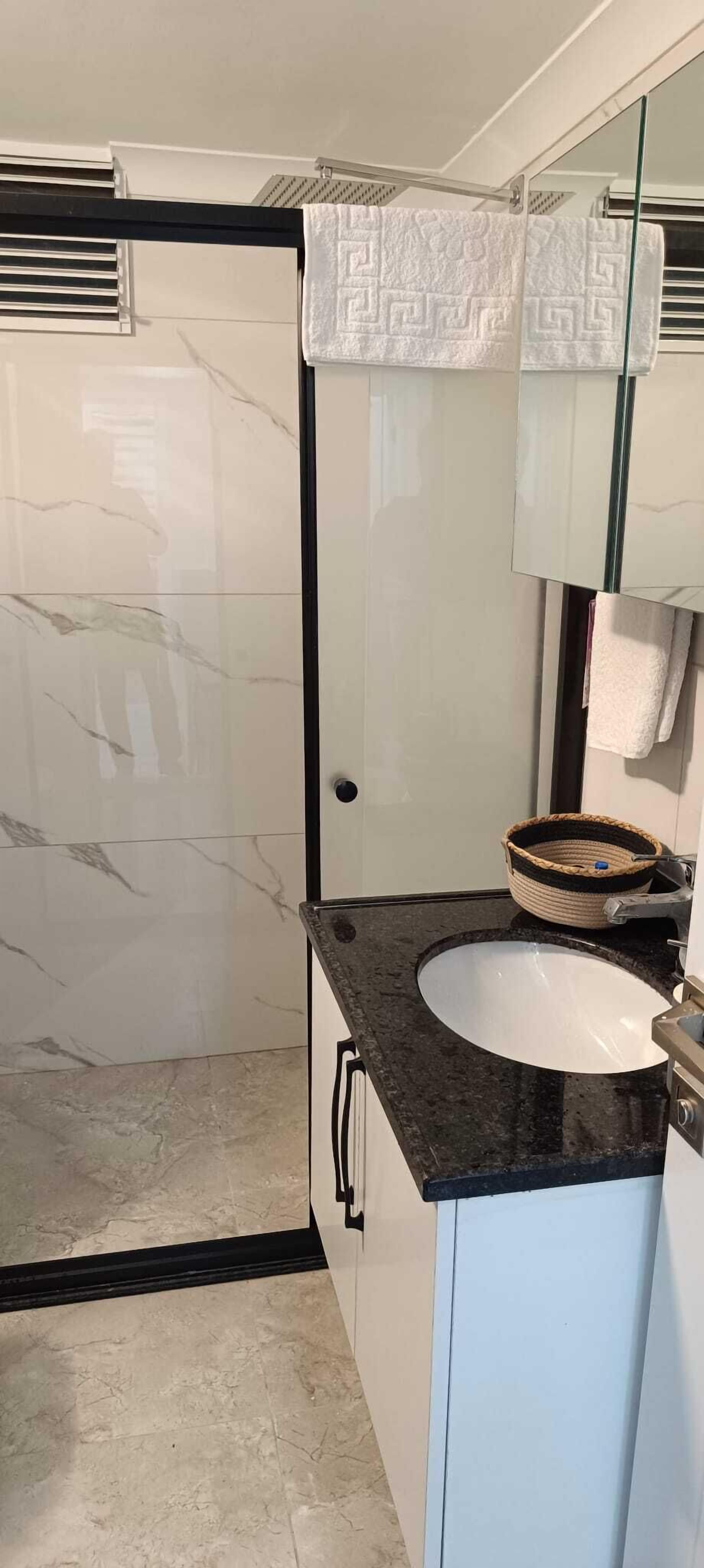 A bathroom with a marble floor, a black countertop, a white sink, and a glass shower enclosure.