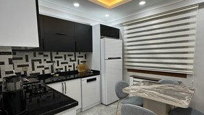 A modern kitchen with a black countertop, white cabinets, and a marble-patterned table. - YASMİNE SUİTE (Trabzon)