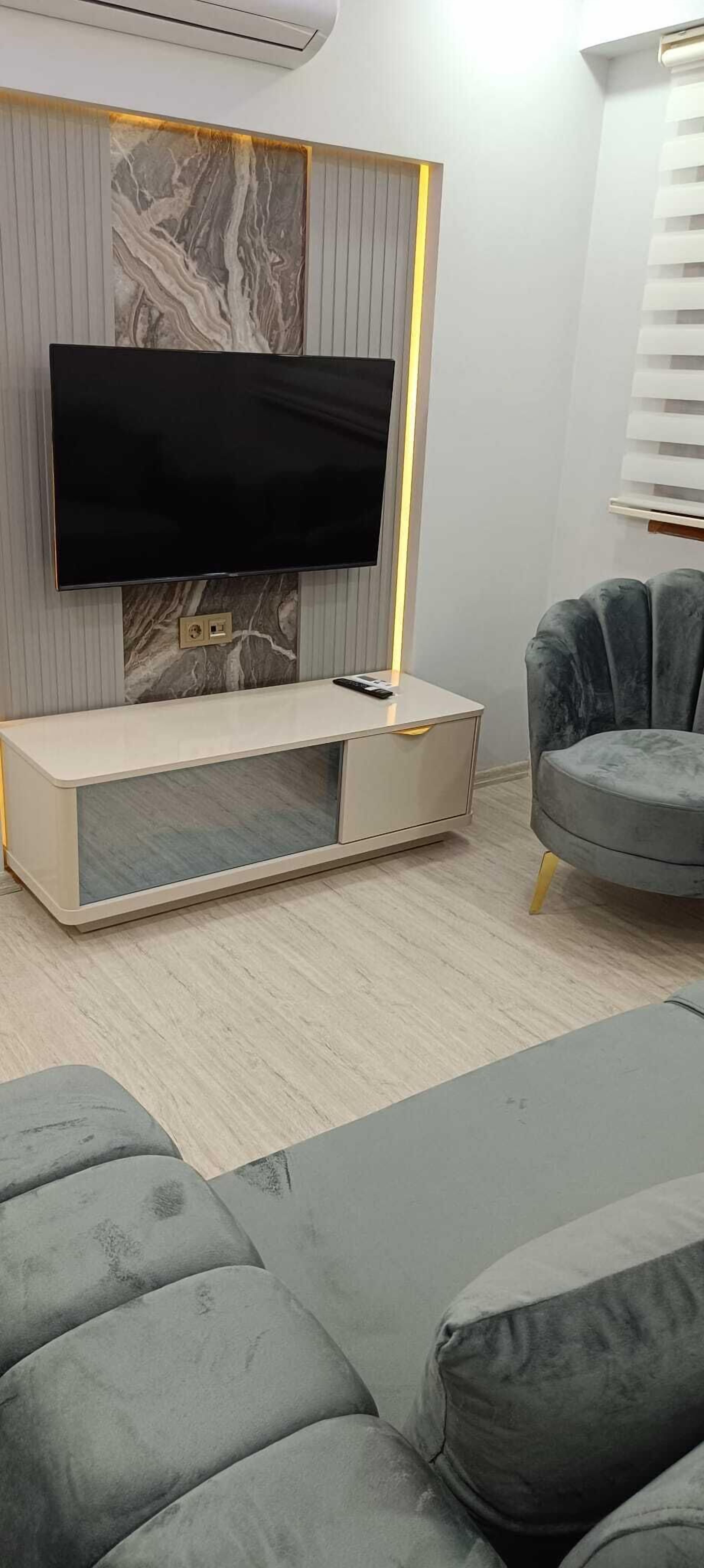 A modern living room with a flat-screen TV mounted on a marble wall, a minimalist entertainment unit, and a grey sofa.