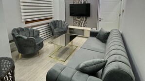 A modern living room with a grey sofa, a glass coffee table, and a TV mounted on the wall. - YASMİNE SUİTE (Trabzon)