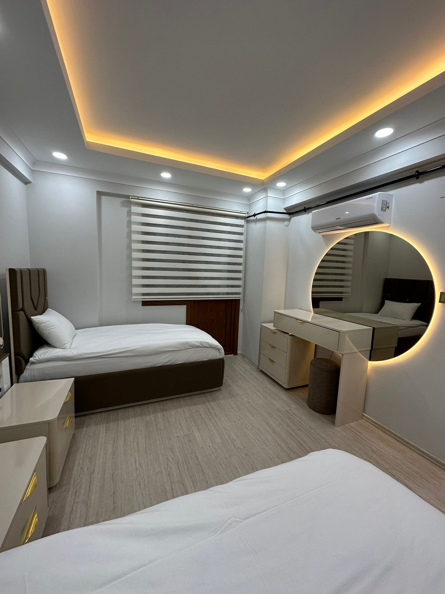 A modern bedroom with a bed, bedside tables, a vanity with a mirror, and a ceiling light fixture.
