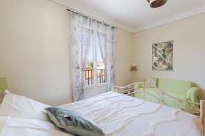 Quarto com cama, janela com cortinas, sofá verde e luminária na parede.