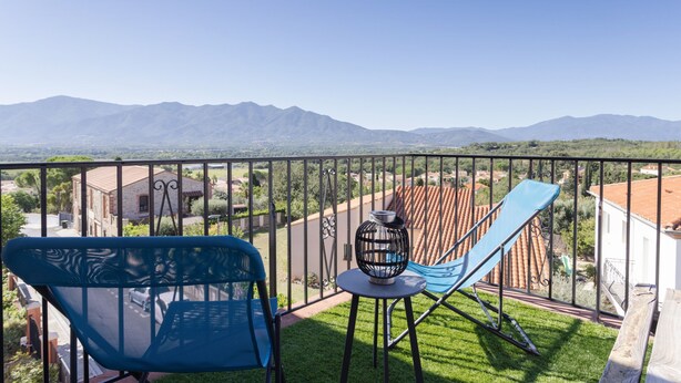A balcony with two chairs, a small table, and a view of distant mountains. - Gîte 'Canigou' with Mountain View, Wi-Fi, and Air Conditioning (Banyuls-dels-Aspres)