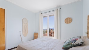 Une chambre à coucher avec un lit, une fenêtre avec des rideaux, un attrape-rêves et une décoration murale tissée.