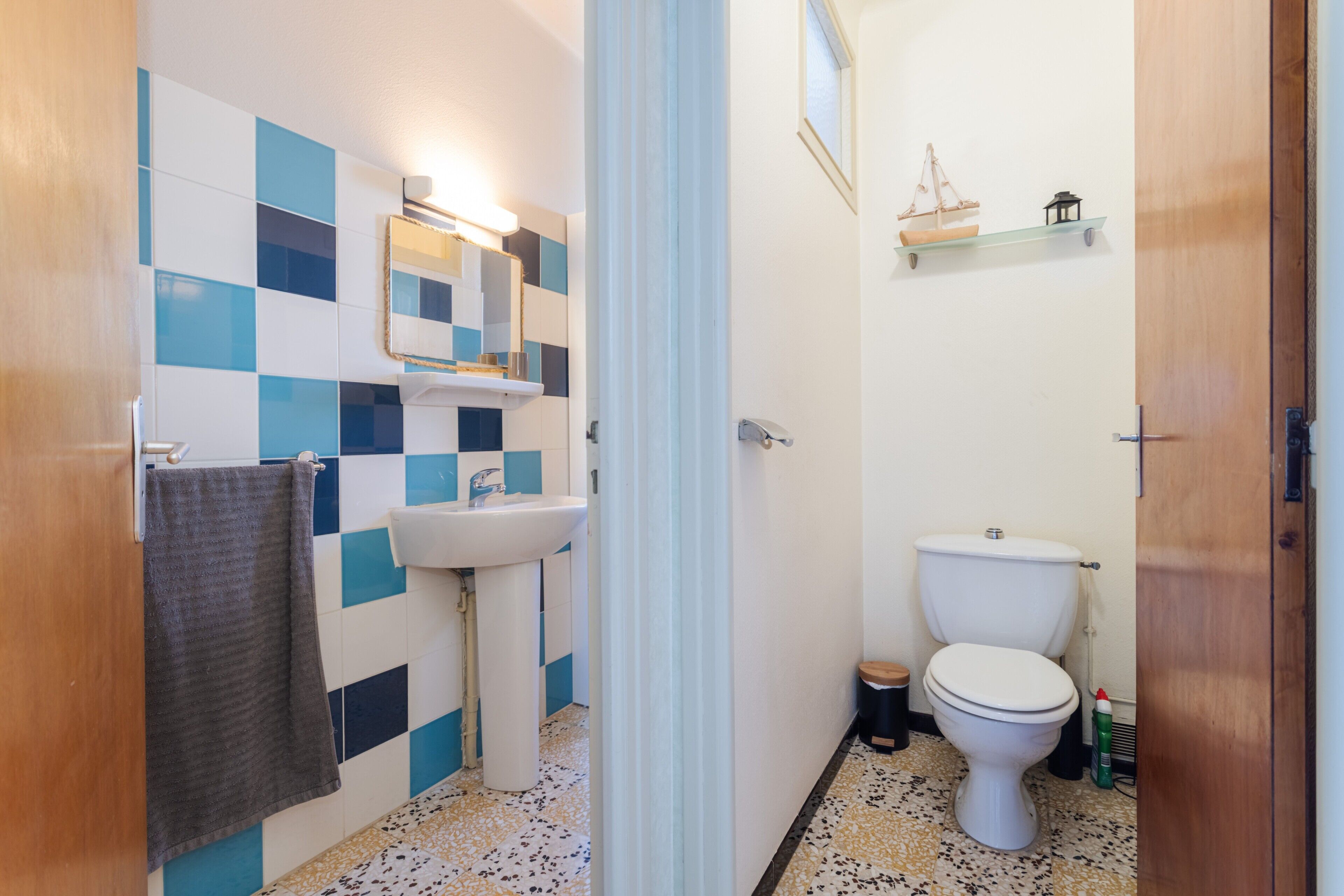 A bathroom with a checkered tile wall, a sink, a toilet, and a mirror.