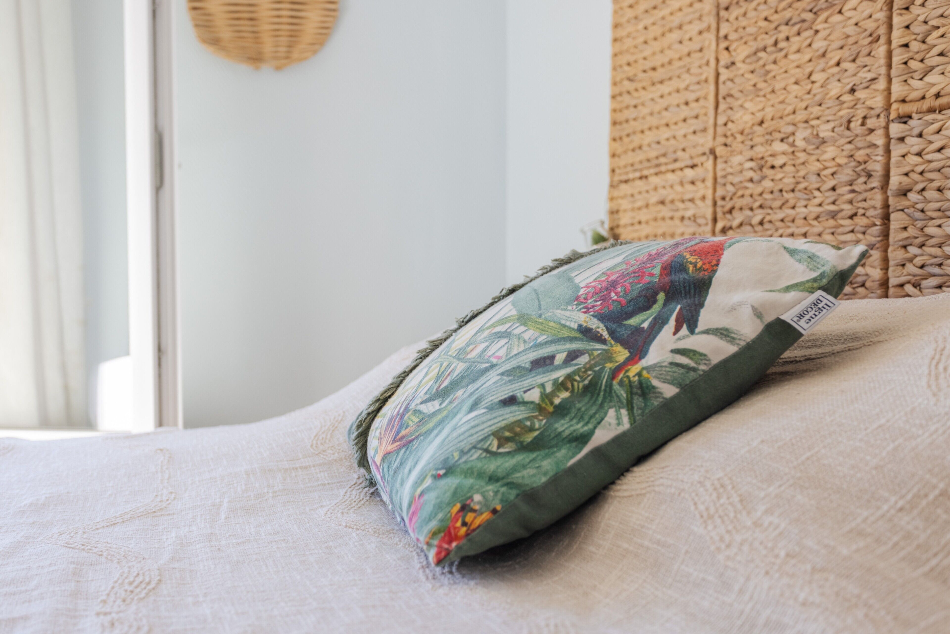 Una cama con un cojín floral, un panel de pared tejido y una puerta blanca.