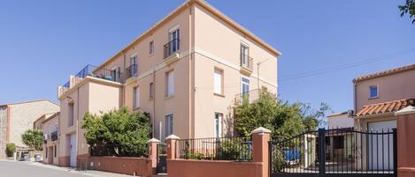 A multi-story residential building with balconies, a gated entrance, and a clear sky.