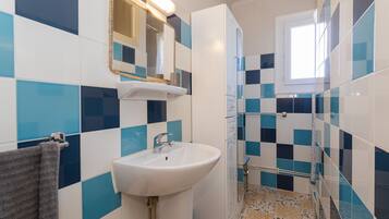 Un baño con lavamanos blanco, un espejo y zona de ducha.