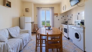 Une cuisine compacte équipée d’un lave-linge, d’une table à manger avec des chaises, d’un canapé et d’un téléviseur fixé au mur.