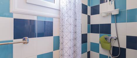 A bathroom with blue and white tiles, a shower with a green grab bar, and a window above the sink.