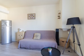 A living room with a sofa, a small table with a plant, a lamp, a refrigerator, and a cabinet.