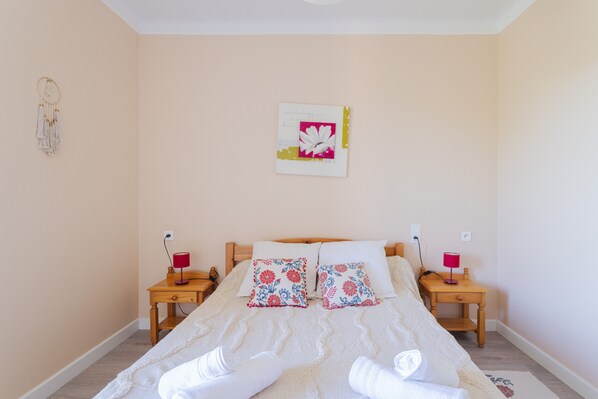 A neatly made bed with floral pillows, a bedside table with a lamp, and a wall decoration.