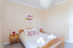 A bedroom with a wooden bed, two bedside tables, a wall-mounted artwork, and a ceiling light fixture.