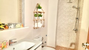 Une salle de bain équipée d’un lavabo, de toilettes, d’une douche et d’une étagère décorative agrémentée de plantes.