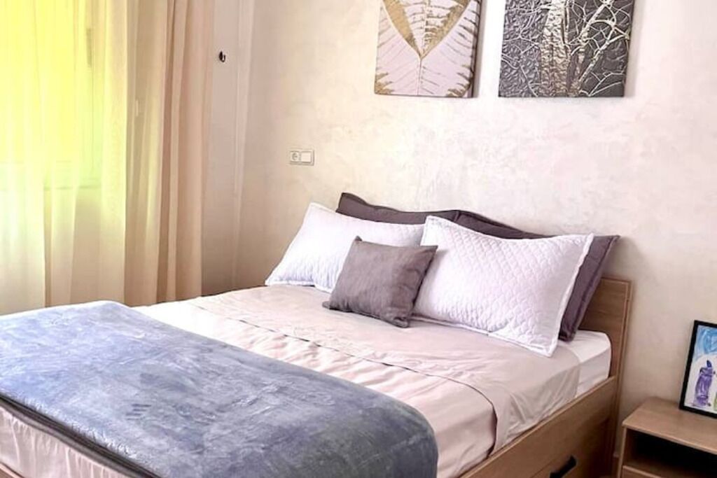 A neatly made bed with a grey mattress and white bedding, a wooden headboard, and two wall-mounted artworks.