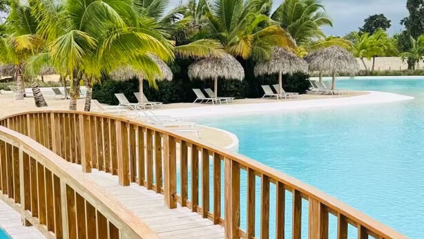 Una terraza de madera que conduce a una piscina con sillas reclinables y palmeras.
