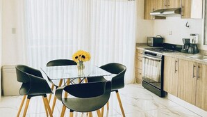 Una cocina moderna con estufa, horno y lavabo. Hay una zona de comedor con mesa y sillas, y un florero con girasoles.
