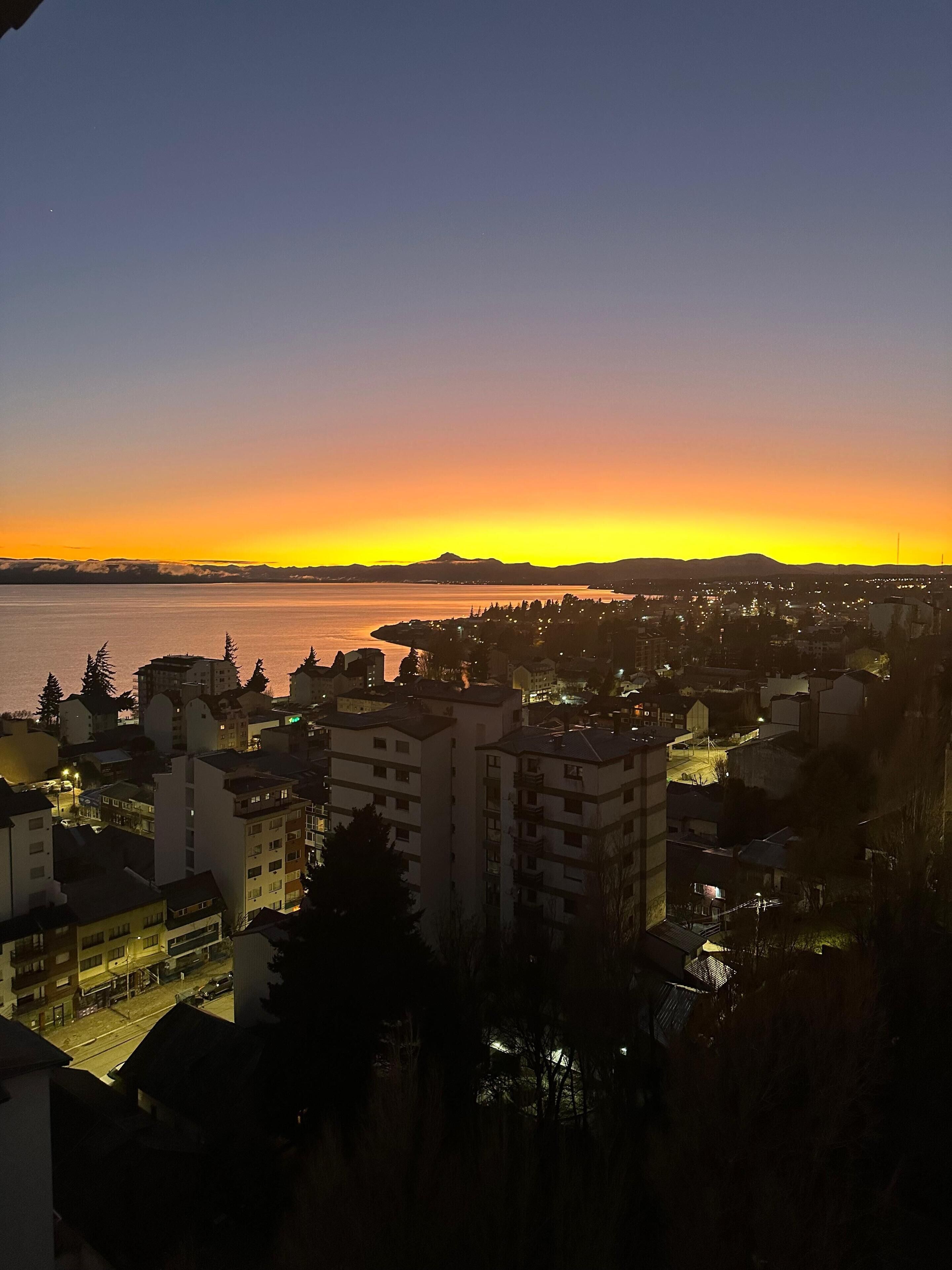 Une vue d’une ville au coucher du soleil, avec des bâtiments et une étendue d’eau en arrière-plan.