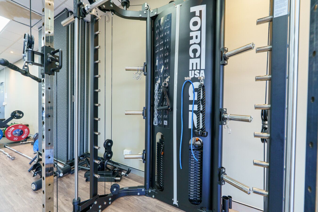 Un gimnasio con zona de levantamiento de pesas, que incluye un rack para sentadillas y diferentes discos de pesas.