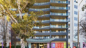 A multi-story building with a modern architectural design, featuring balconies on each floor and a glass entrance.