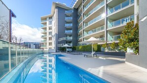A modern hotel with a swimming pool, multiple balconies, and a well-maintained outdoor area with lounge chairs.