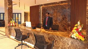 A reception desk with a marble surface, two black office chairs, and a man in a suit standing behind it. - Hotel National Park  (Kottayam)