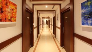 A hotel hallway with multiple doors, framed artwork on the walls, and a polished floor. - Hotel National Park  (Kottayam)