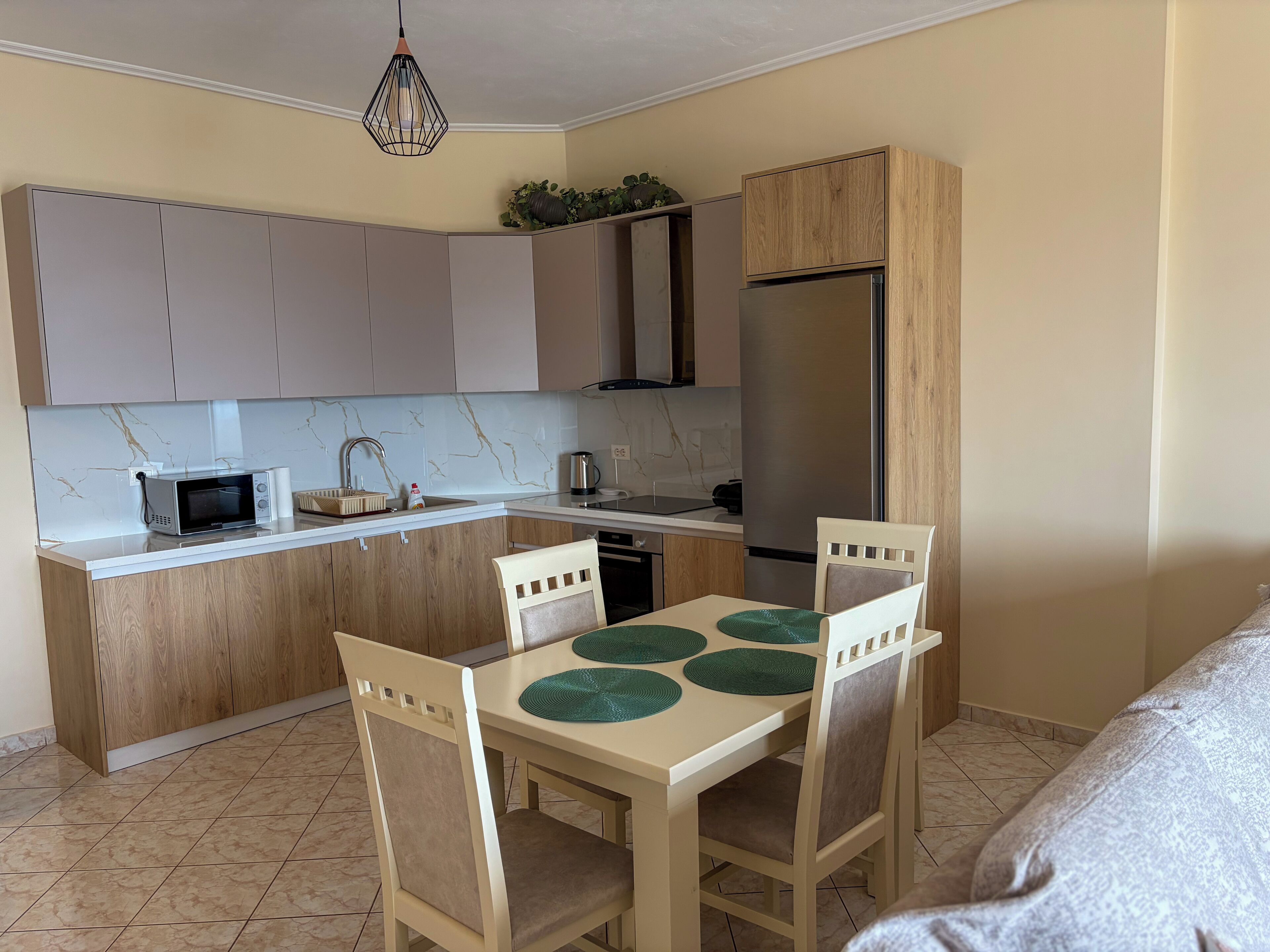 Uma cozinha compacta com ilha central, armários de madeira, micro-ondas embutido e geladeira de aço inoxidável.