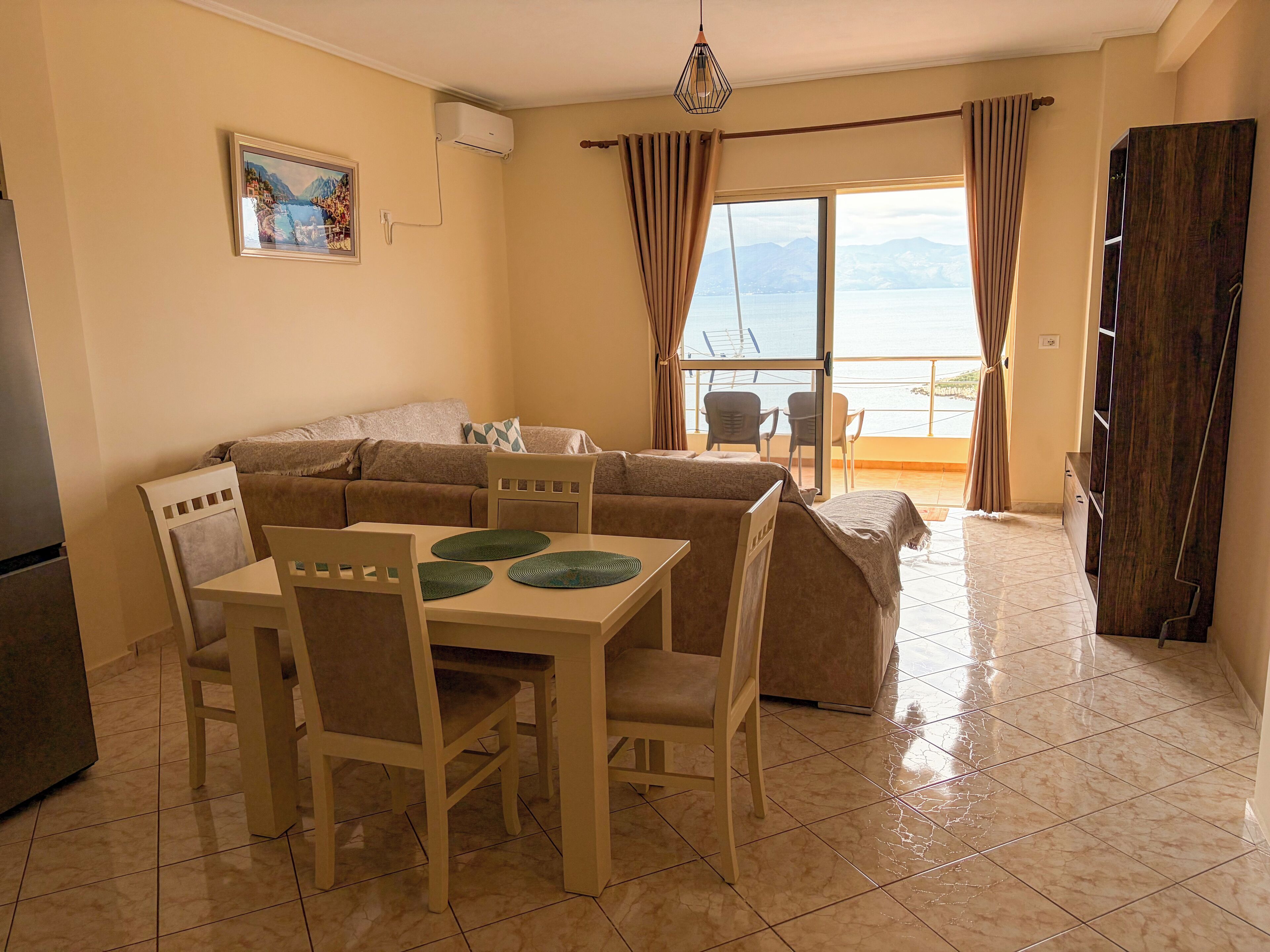 A living room with a sofa, dining table, chairs, and a view of the sea through a large window.