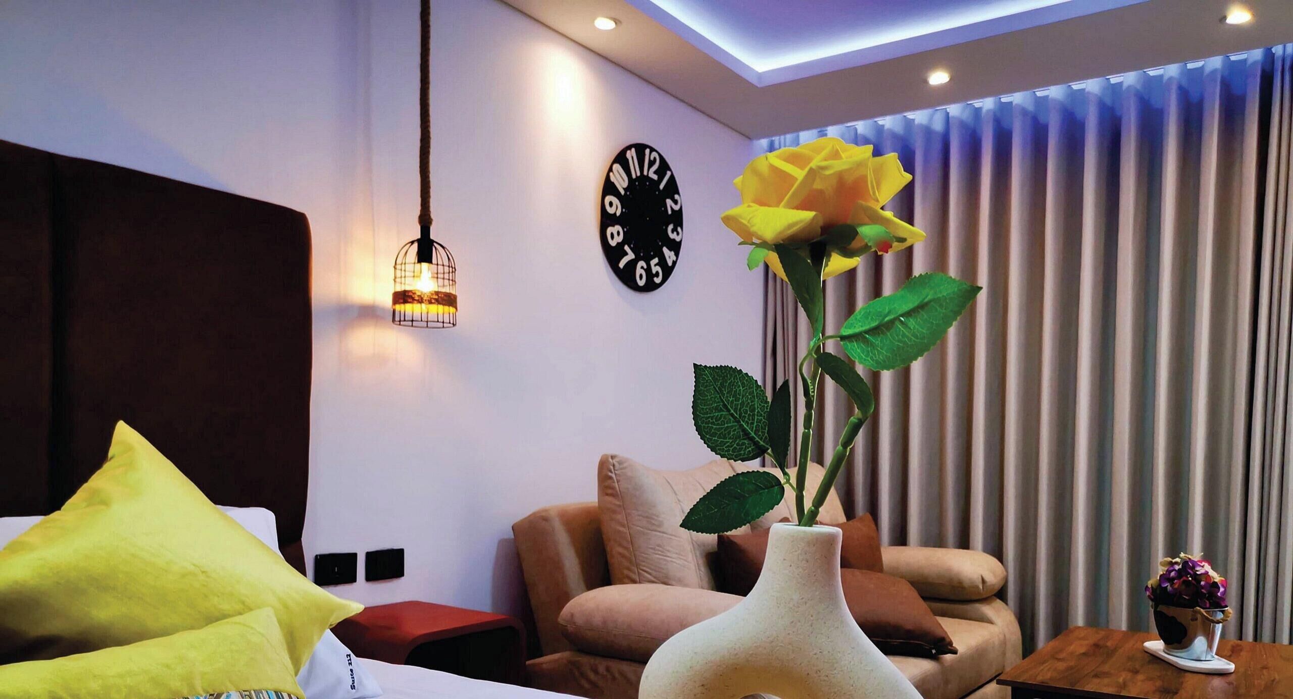 Una sala de estar moderna con un sofá, un jarrón amarillo con una rosa, un reloj y una ventana con cortinas.