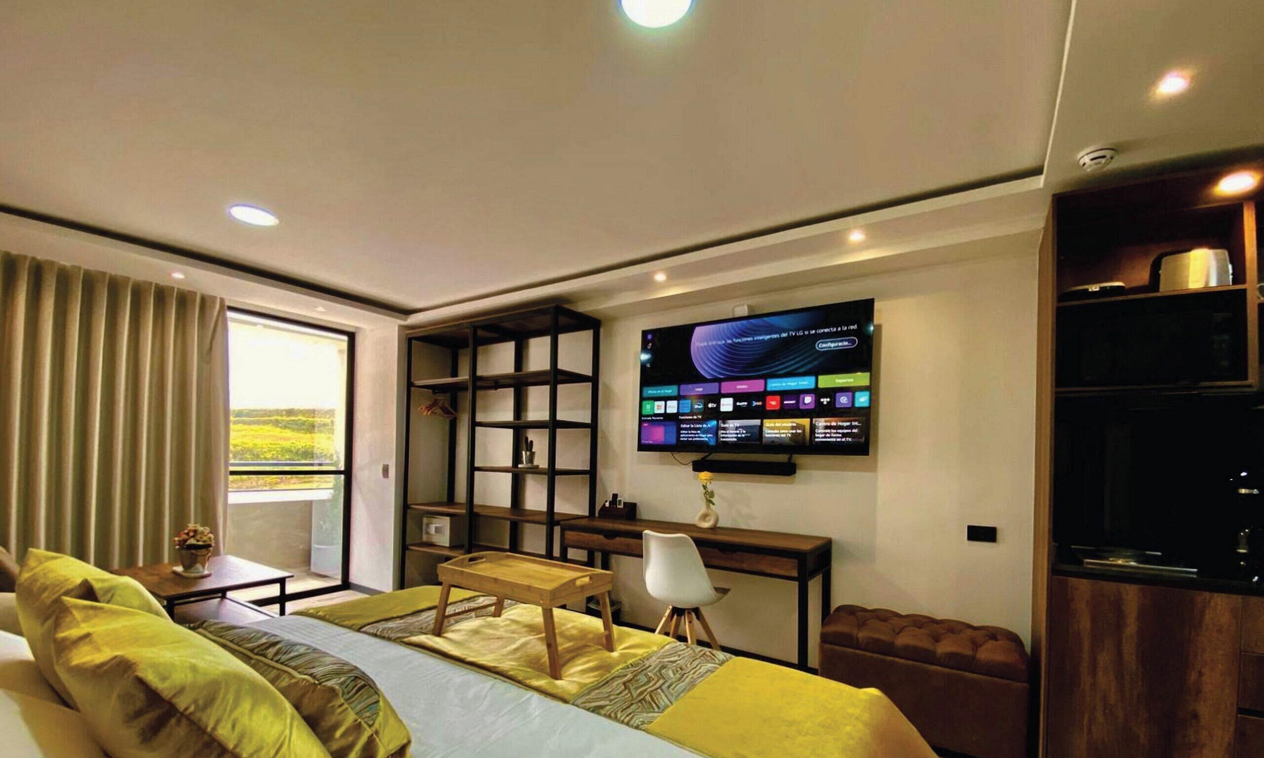 A modern hotel room with a bed, a desk, a chair, and a TV mounted on the wall.