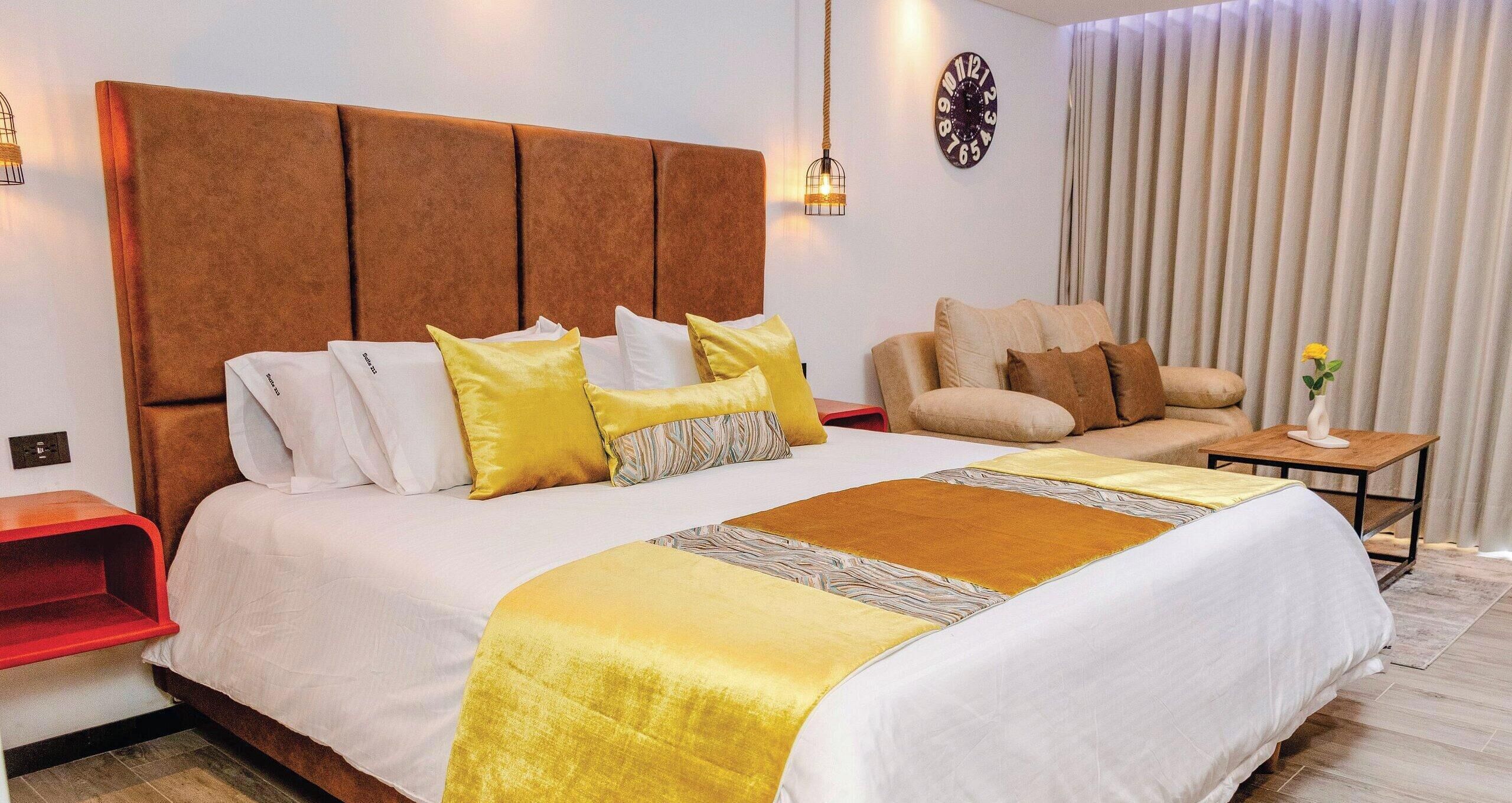 A hotel room with a large bed, a sofa, a small table, and a clock on the wall.